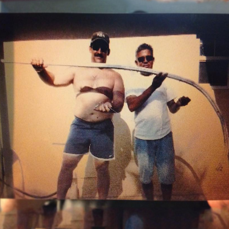 Two Men Holding A Curved Metal Bar, Posing For A Photo